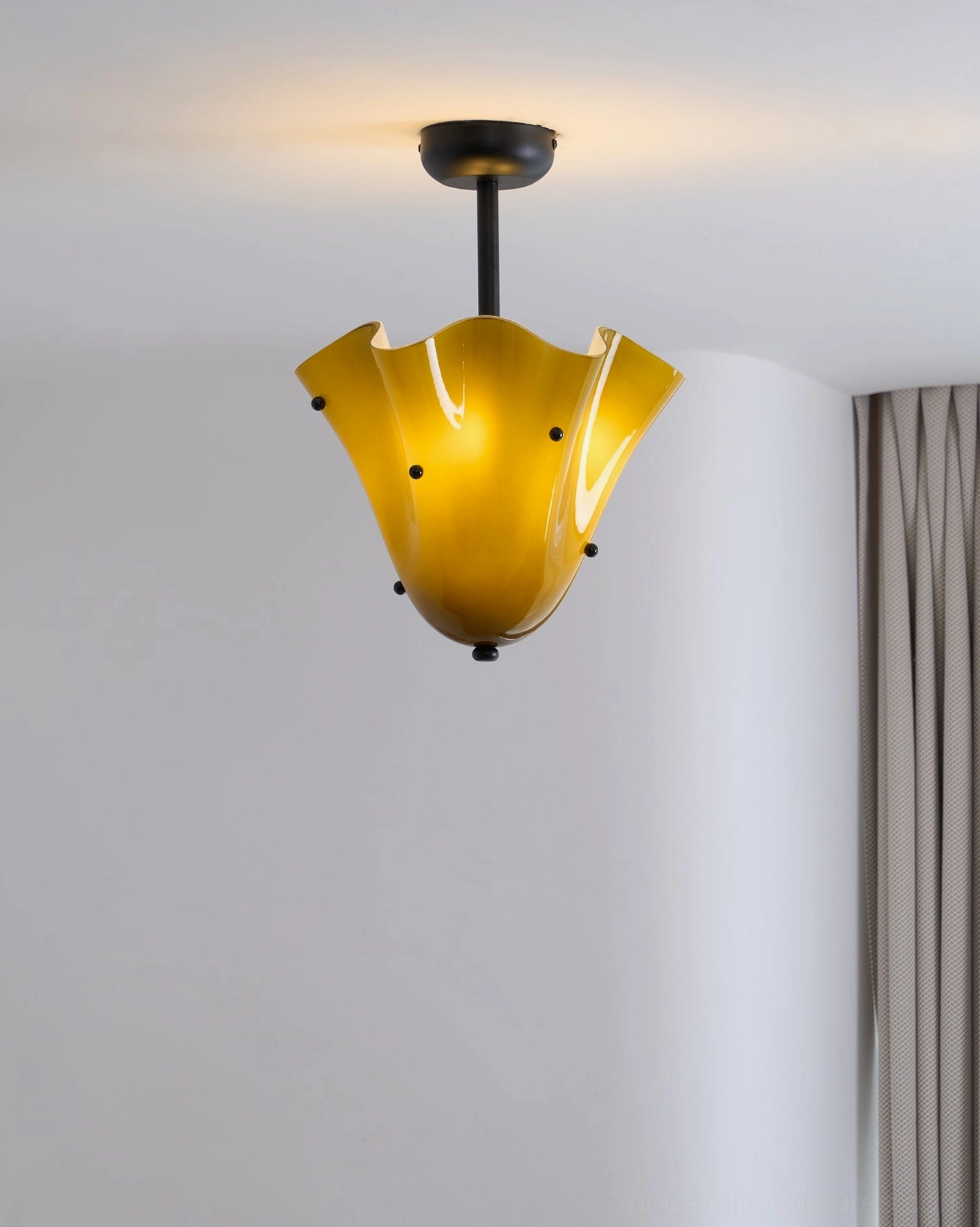 Vera ceiling light glowing warm amber in minimalist gray bedroom with curtains