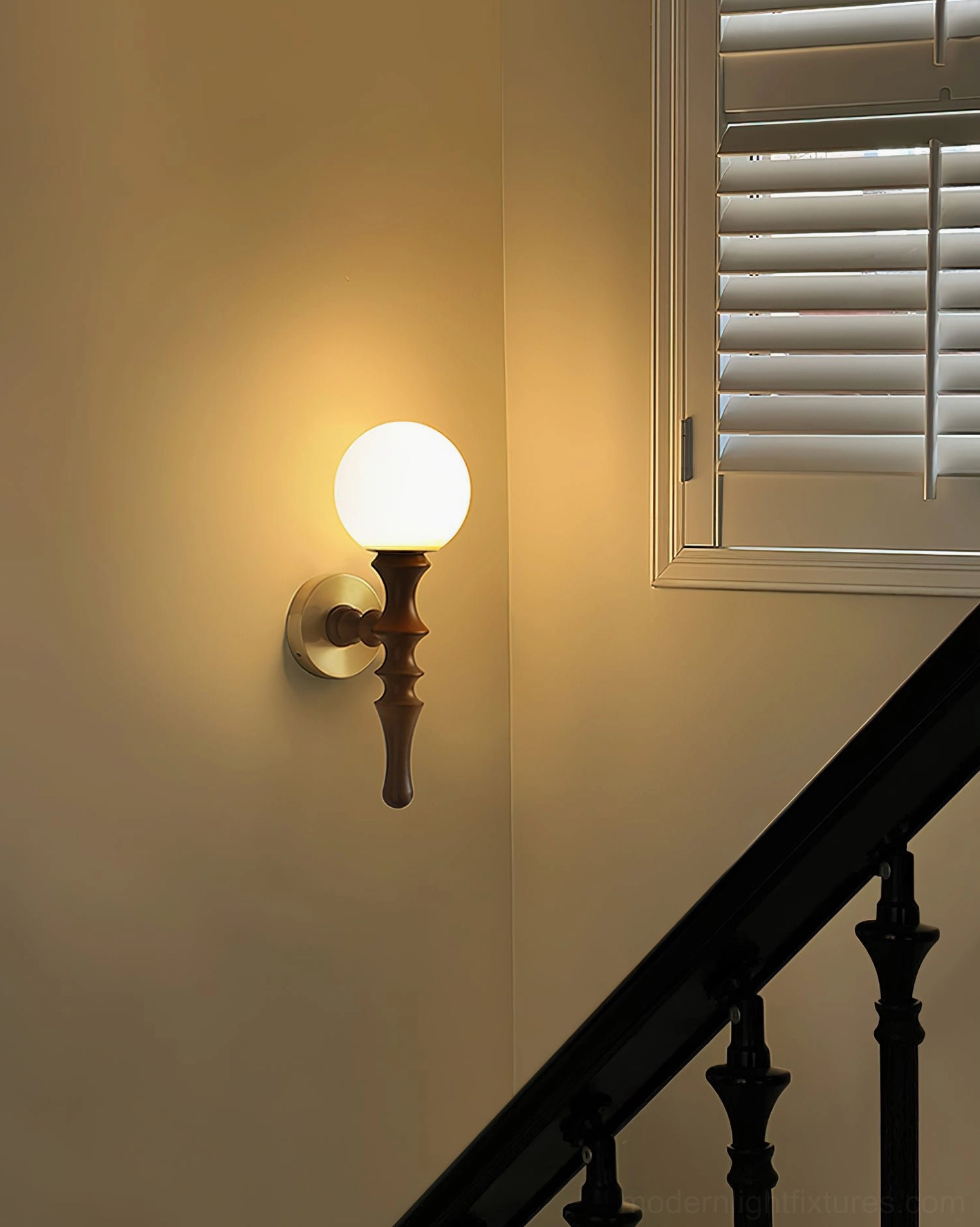 Illuminated Vero wall sconce mounted on dark wooden staircase with warm glowing frosted glass globe
