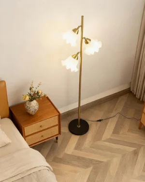 Vervina botanical floor lamp in bedroom setting with herringbone wood floor and warm brass finish illuminated petal shades
