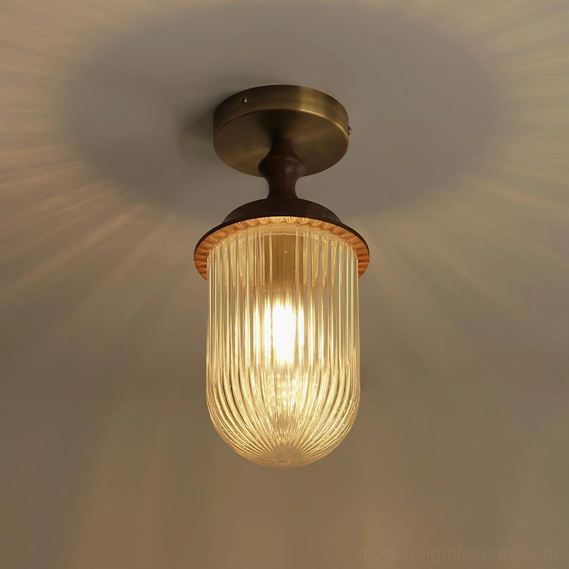 Illuminated Veyra modern ceiling lamp casting warm radial light patterns from ribbed glass sphere and brass mount