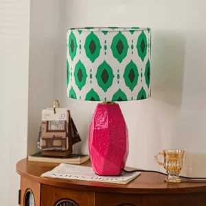 Vico bohemian geometric table lamp with rose pink textured ceramic base and green diamond print shade, three-quarter view on vintage wooden side table