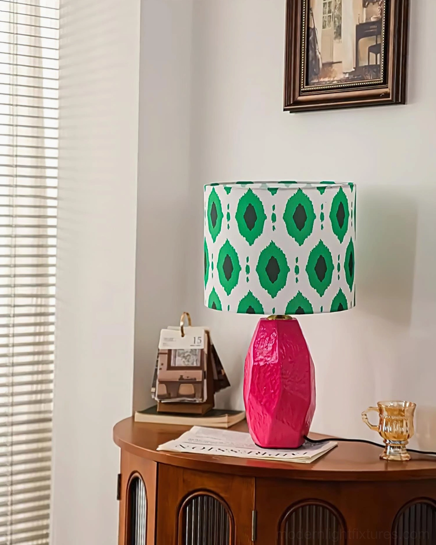 Vico bohemian table lamp with rose pink faceted ceramic base and green geometric ikat shade, three-quarter view with window blinds backdrop