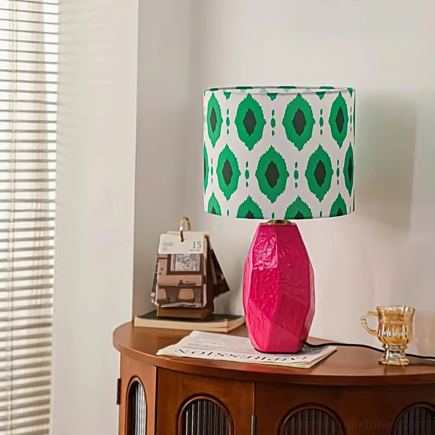 Vico modern table lamp with textured pink ceramic base and green geometric fabric shade, side view near window with blinds