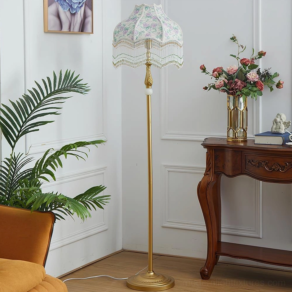 Victorian floor lamp with gold metal pole and white floral shade beside wooden table
