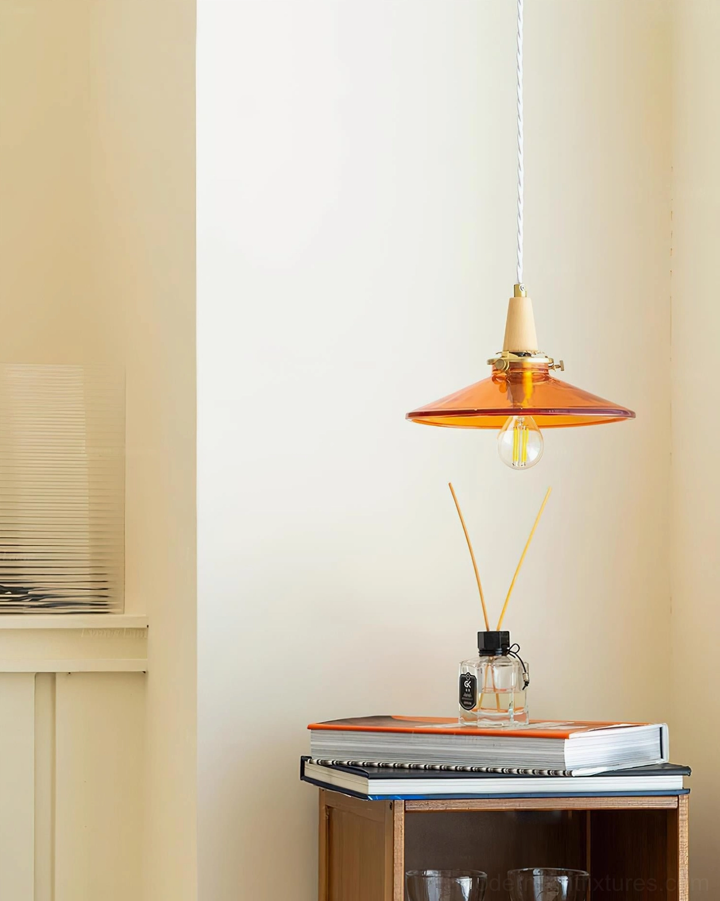Vintage amber pendant light above side table with decorative books and accessories, low angle perspective