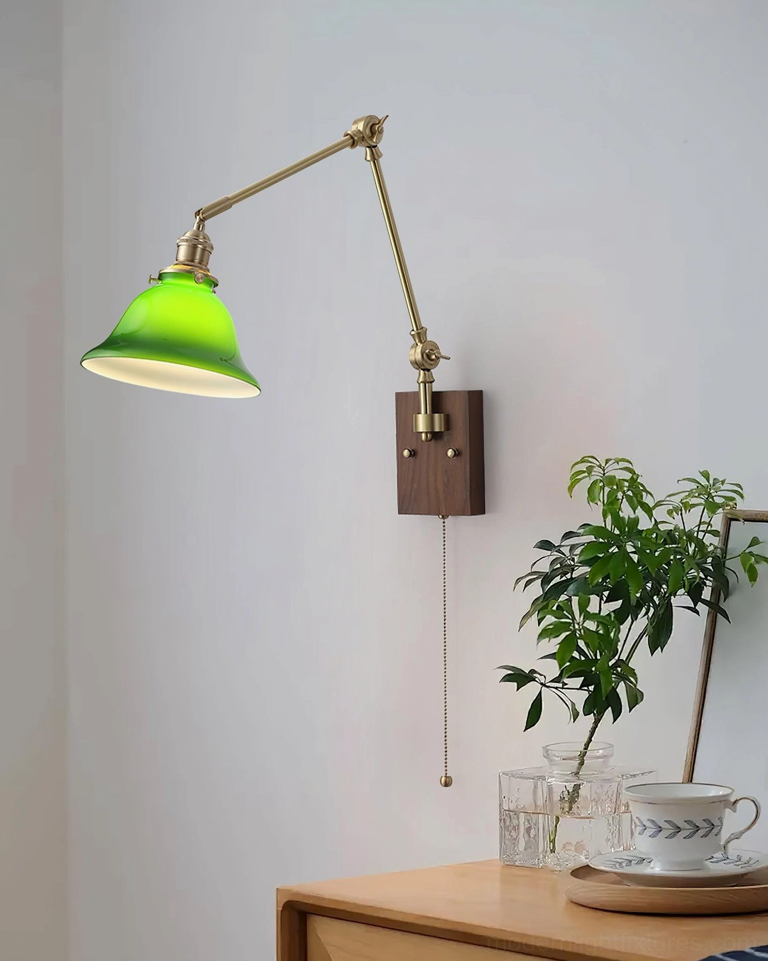 Vintage banker's lamp style swing arm wall sconce with brass framework and green glass shade, showing articulated arm design and wood backplate
