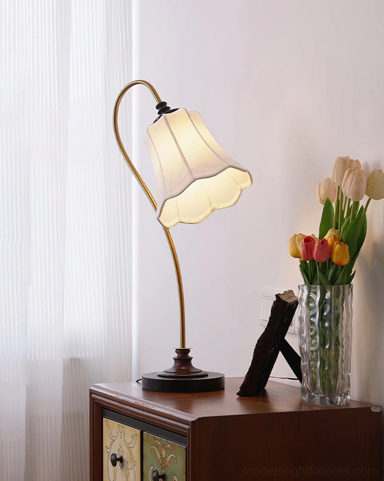 Vintage brass arm table lamp with dark wooden base on bedroom nightstand with fresh flowers