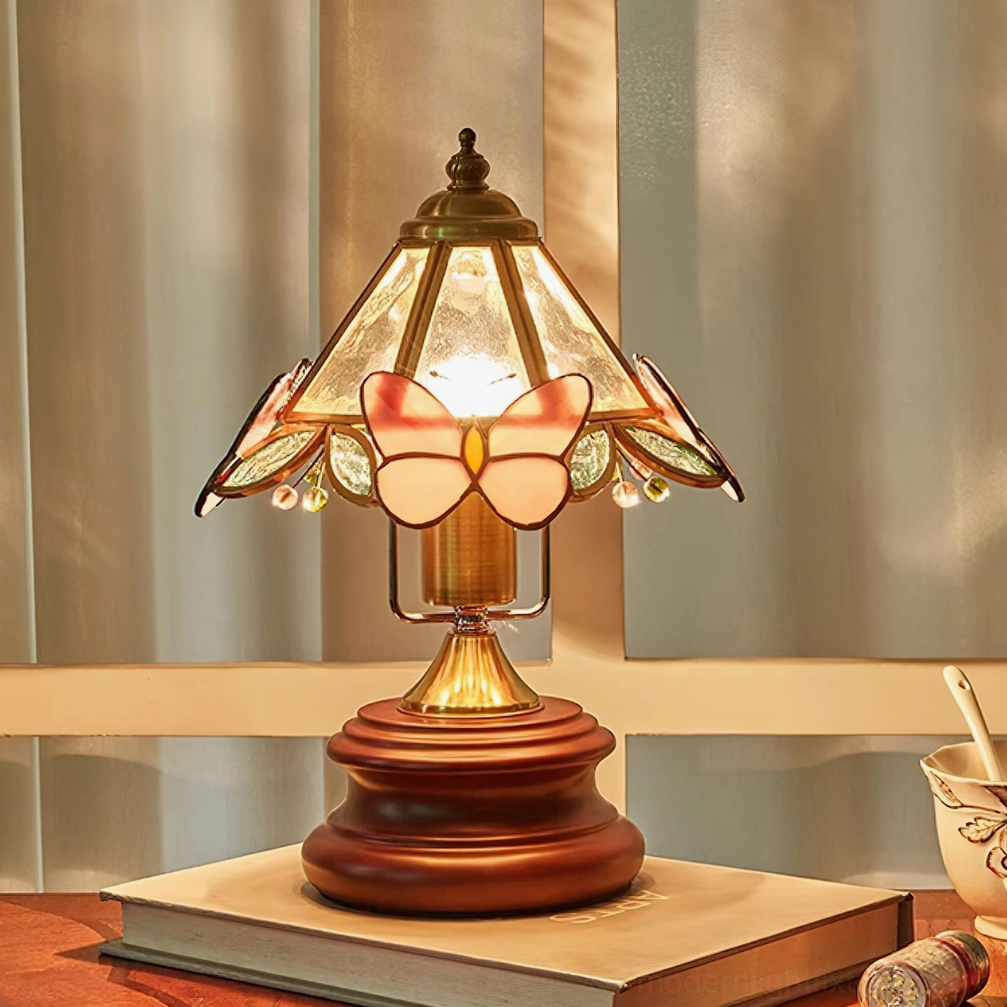 Stained glass butterfly table lamp on tabletop with stacked books and teacup showing decorative brass hardware