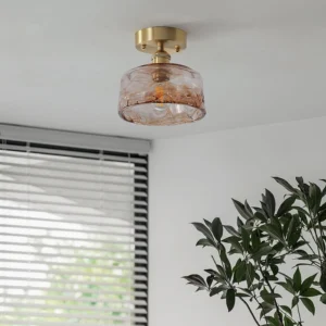 Vintage semi-flush ceiling light mounted overhead in bright room with plant and window blinds, showing brushed brass and marbled amber glass