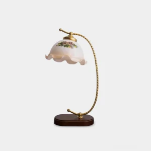Vintage floral table lamp with curved brass stem and ruffled glass shade, side view on white background