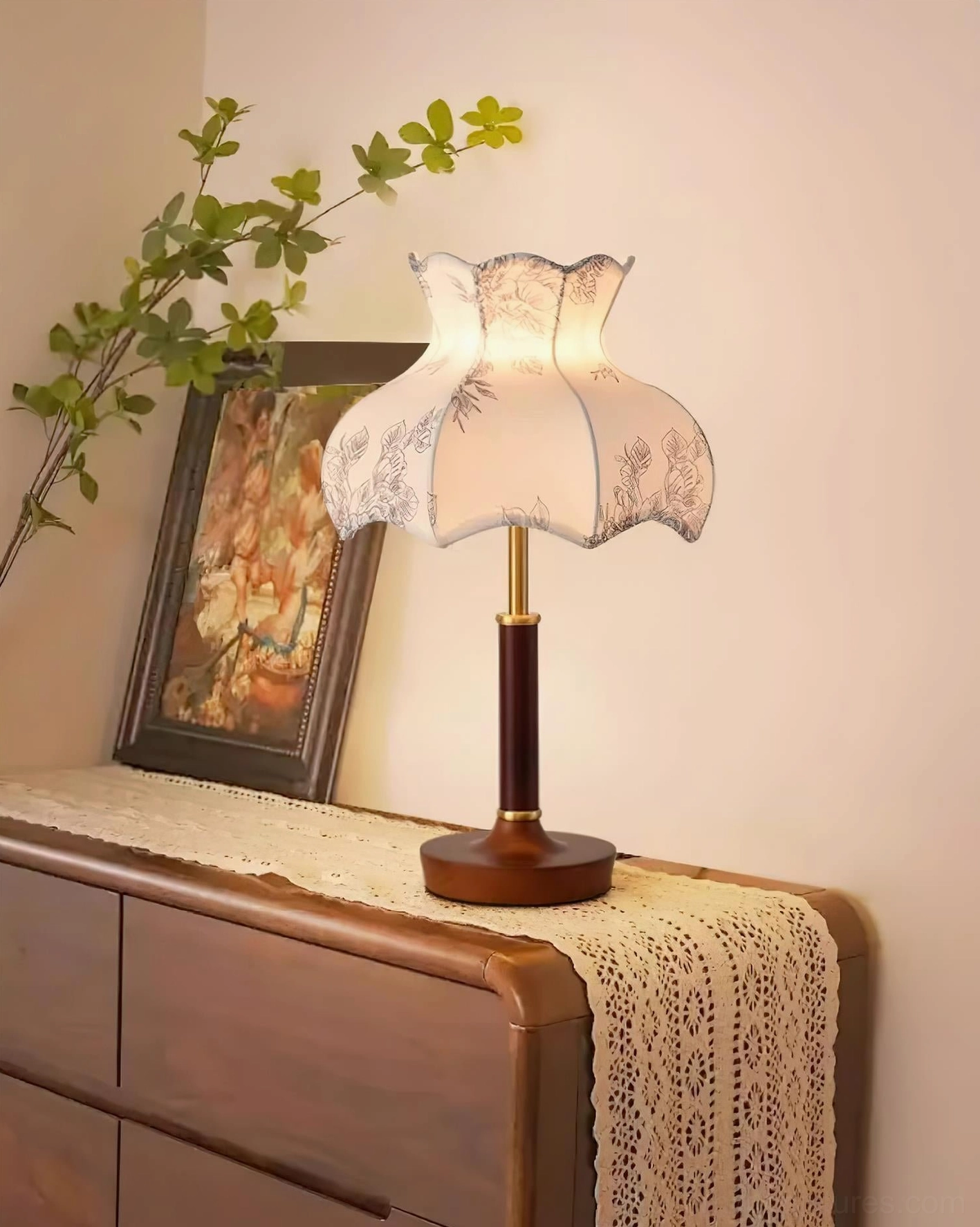 Antique style floral table lamp with scalloped fabric shade on retro dresser, styled with framed art and greenery