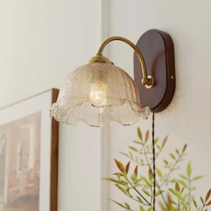 Vintage flower wall sconce with warm amber textured ruffled glass shade mounted on residential wall with glowing bulb inside