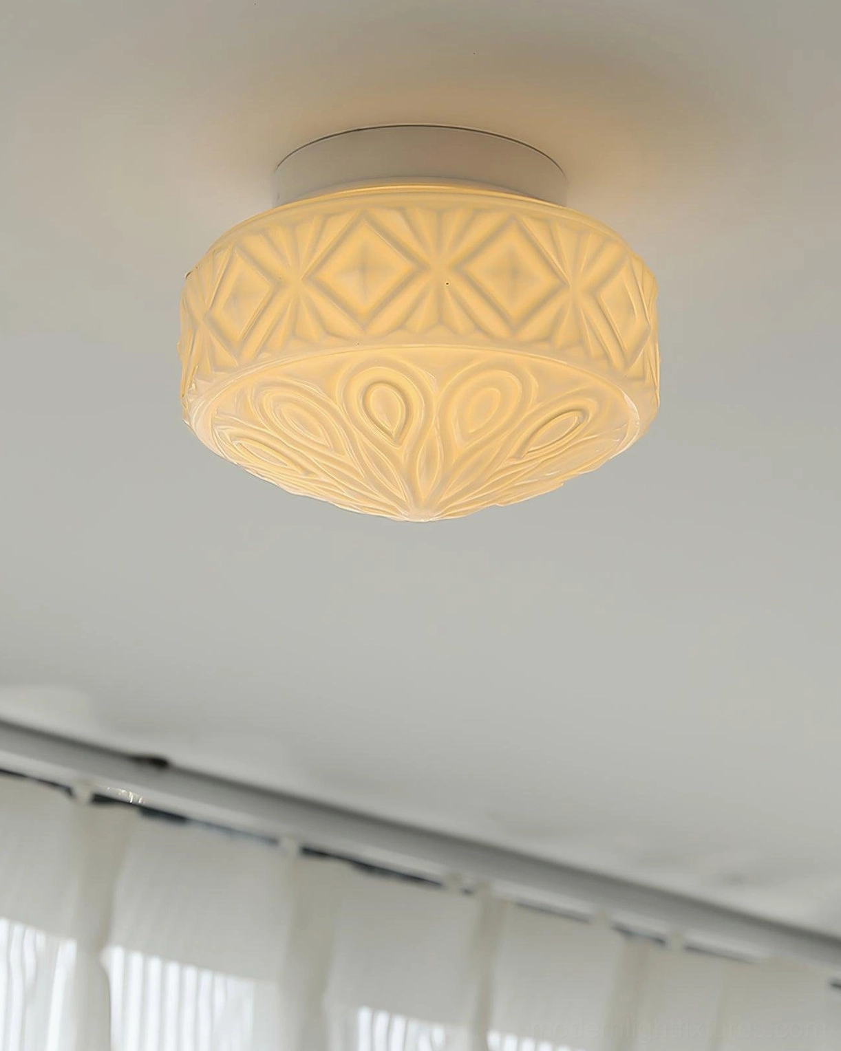 Installed lit embossed glass ceiling light casting warm glow in interior room with window curtains and vintage fixture design