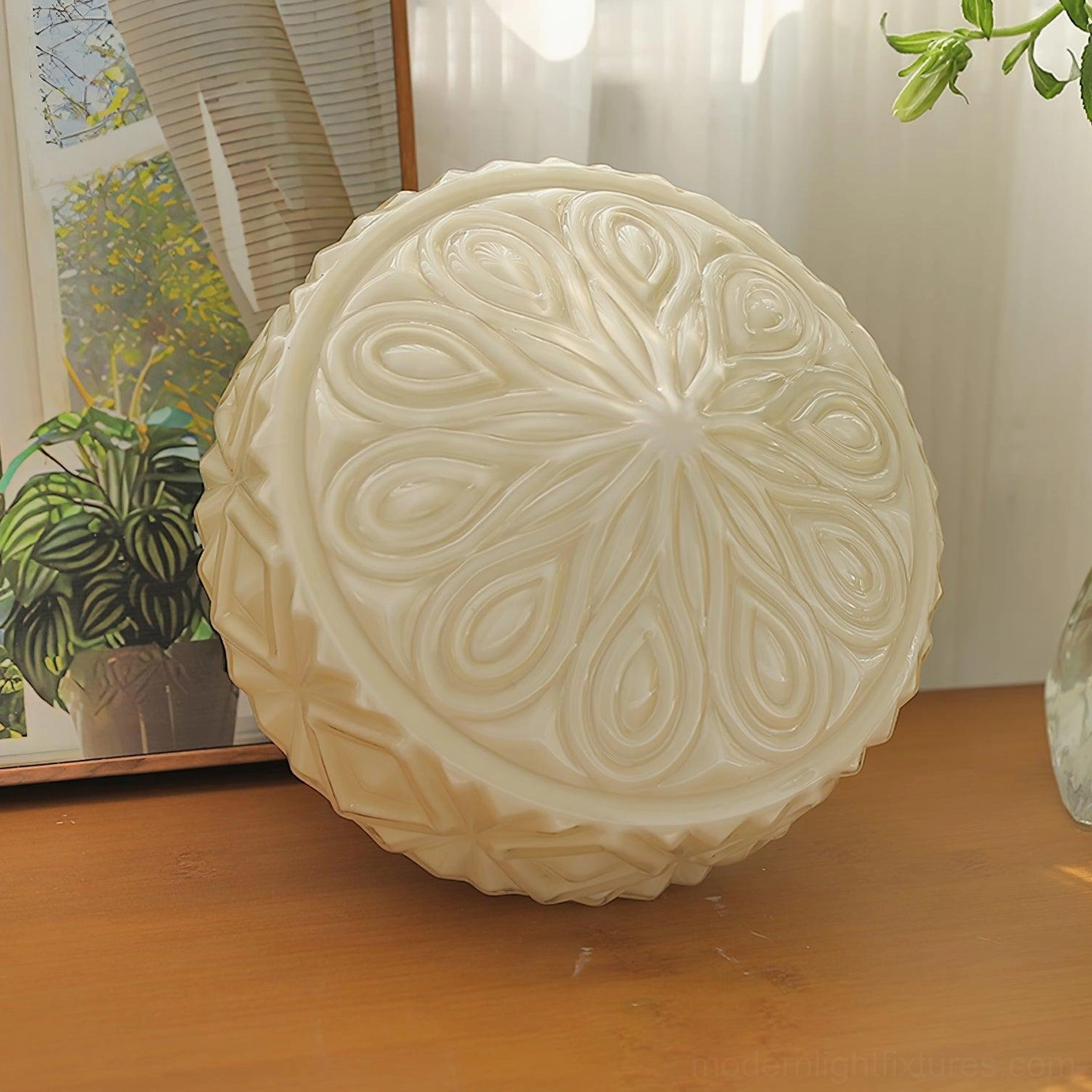 Uninstalled vintage carved glass ceiling fixture showing radial scroll pattern in cream white, overhead tabletop view with greenery