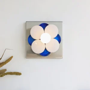 Close-up of Violetta wall sconce with frosted white petals and blue accents, mounted on white wall with dried botanical decor