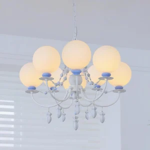 8-head Vionette chandelier with white metal arms, pastel blue accents, frosted glass globes, and crystal pendants against indoor background with window shutters