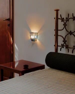 Contemporary wall sconce with vintage stained glass shade installed in bedroom above nightstand, warm ambient lighting