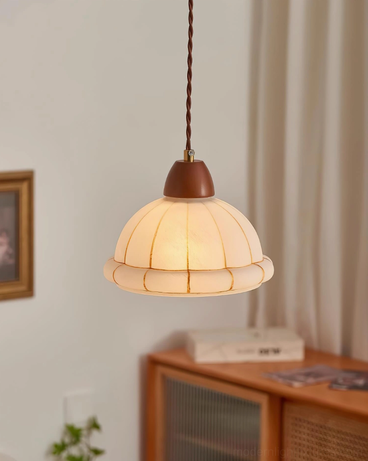 Kaya glass pendant lamp suspended in corner room with curtain, wooden cabinet and decorative plant