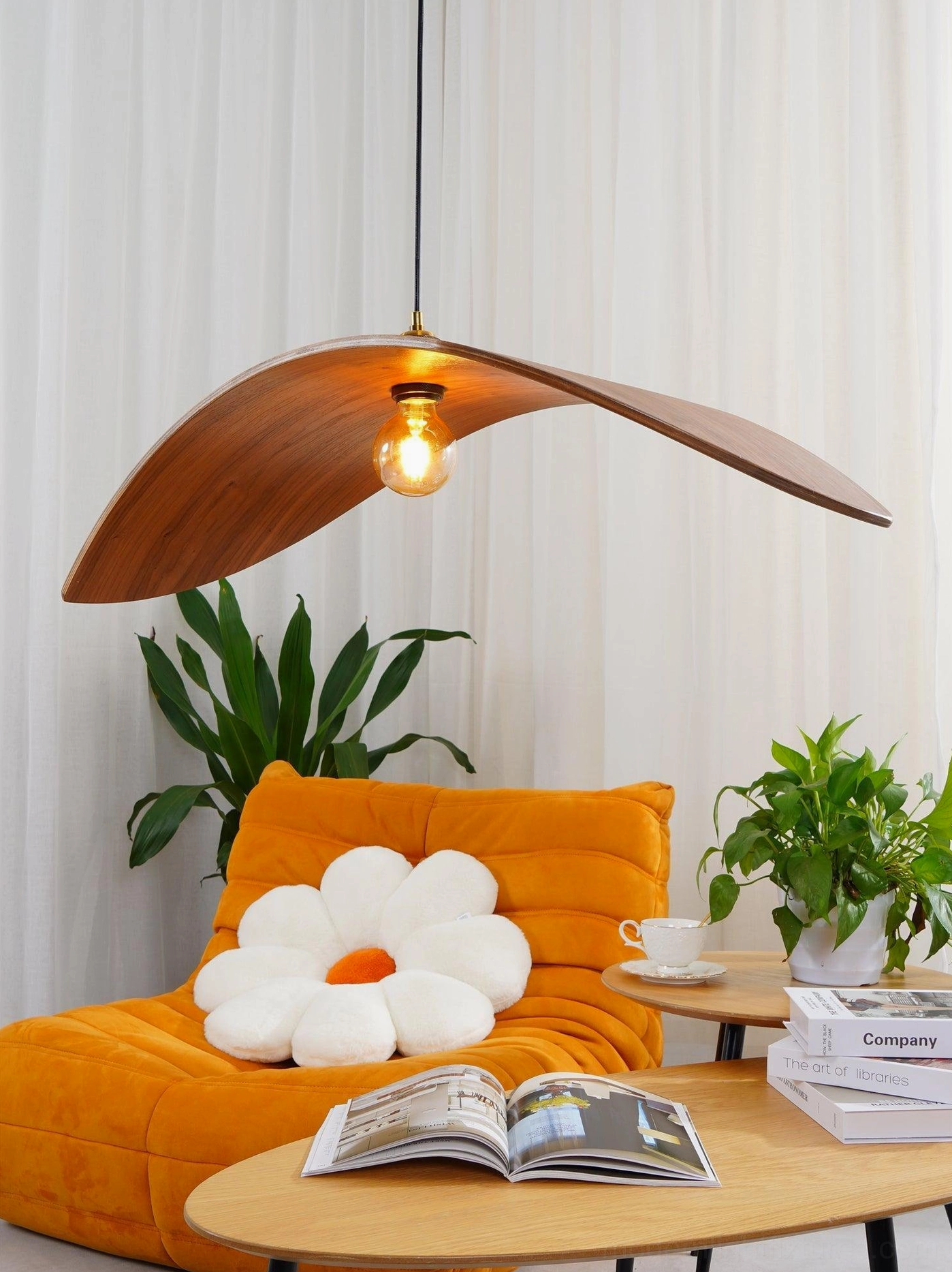 Three-quarter side view of walnut wood leaf pendant lamp in bright living room with curved light brown wood shade and exposed vintage bulb