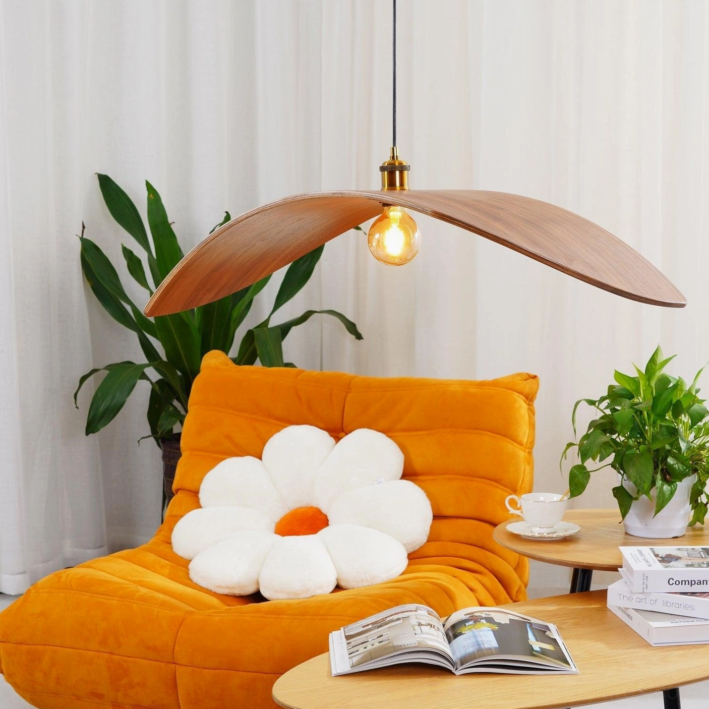 Low-angle perspective of walnut wood leaf pendant lamp in cozy living space with orange sofa showing warm ambient lighting and natural wood grain