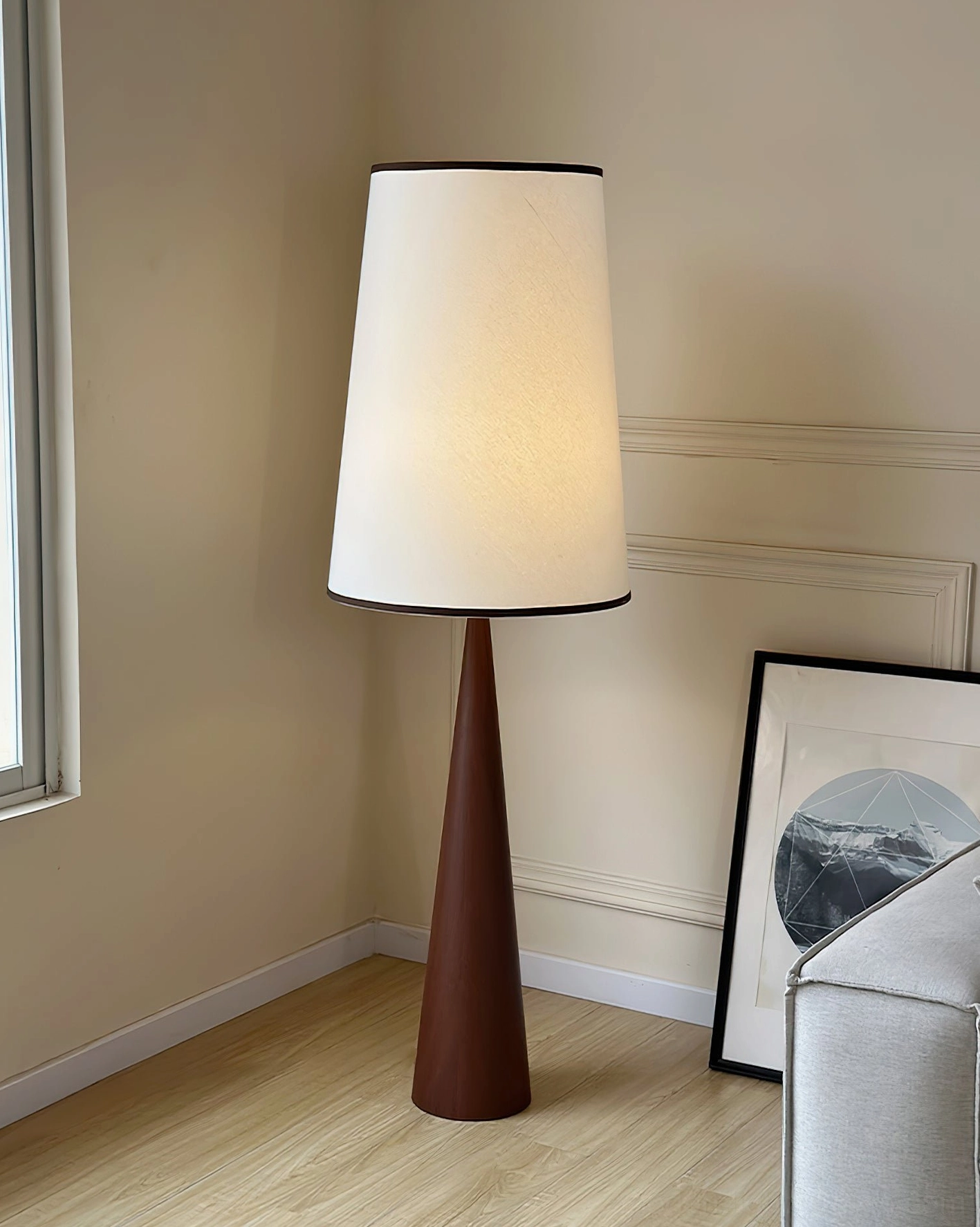 Dark walnut tapered floor lamp illuminated in corner of wainscot living room beside upholstered sofa