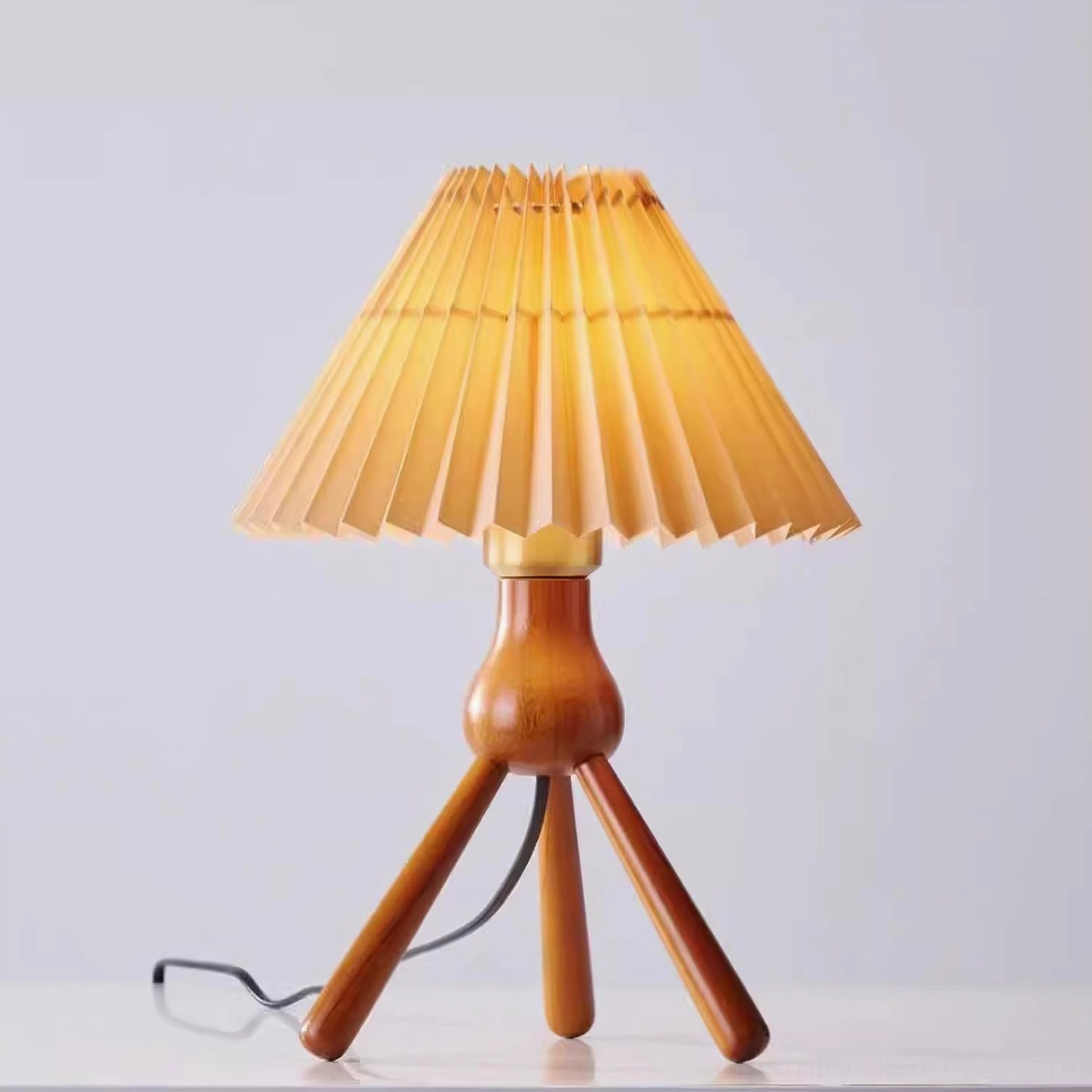 Dark walnut wood tripod table lamp with pleated shade and power cord visible, three-quarter view