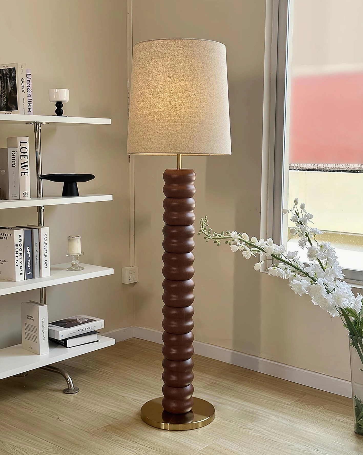 Dark walnut stacked wood floor lamp with brass base beside bookshelf, side angle view