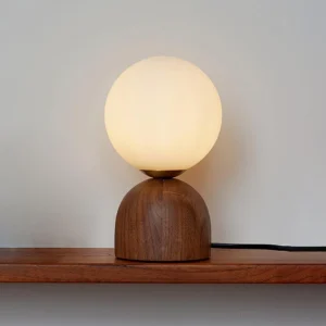 Walnut wood table lamp with frosted glass sphere shade displayed on wooden shelf in home interior