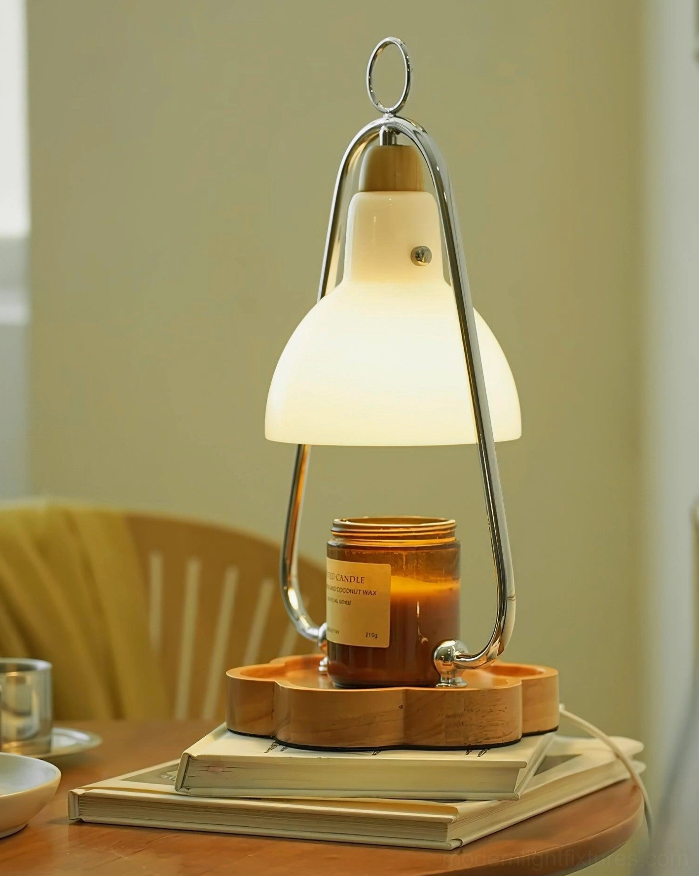 Glowing candle warmer lamp on dining table creating warm atmosphere with stacked books