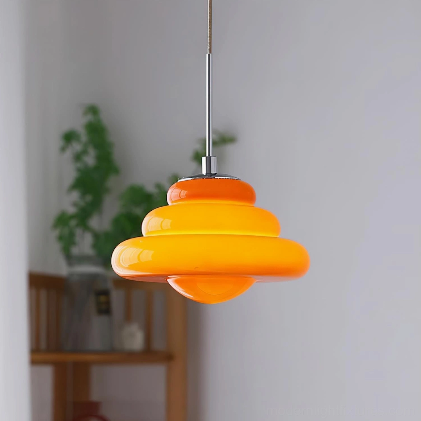 Deep warm orange tiered pendant light suspended above wooden shelf with decorative green plants