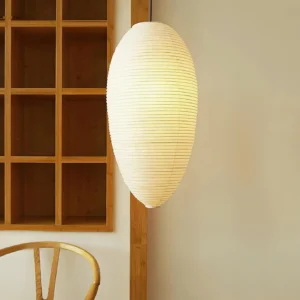 Illuminated washi paper pendant lamp in warm glow, three-quarter angle, displayed in rustic minimalist interior with wooden shelf