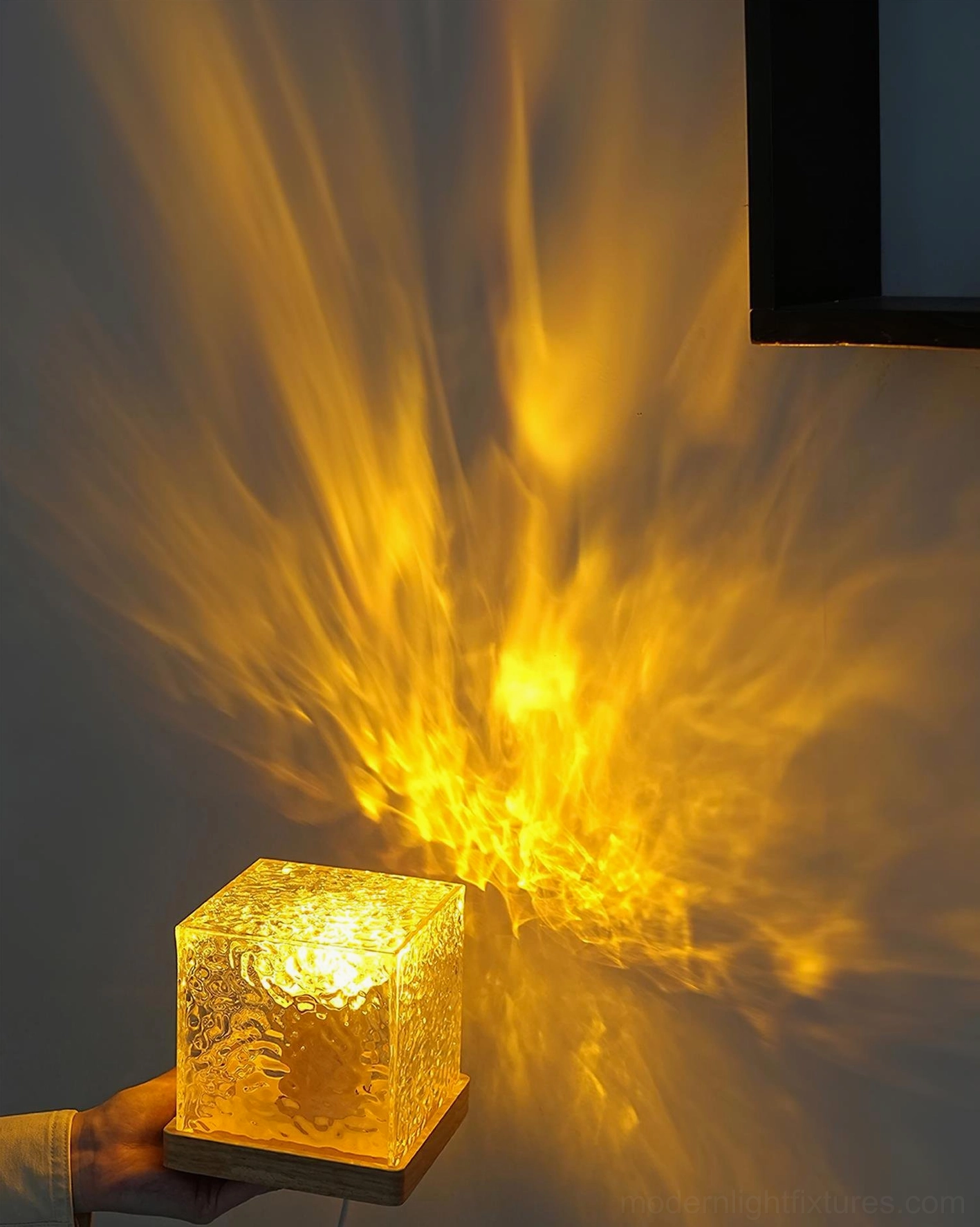 Close-up handheld view of water ripple crystal table lamp showing textured glass cube and glowing amber LED illumination