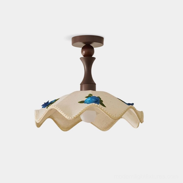 Front low-angle view of wavy scalloped ceiling lamp with hand-embroidered floral details and pastoral fabric shade against white studio background