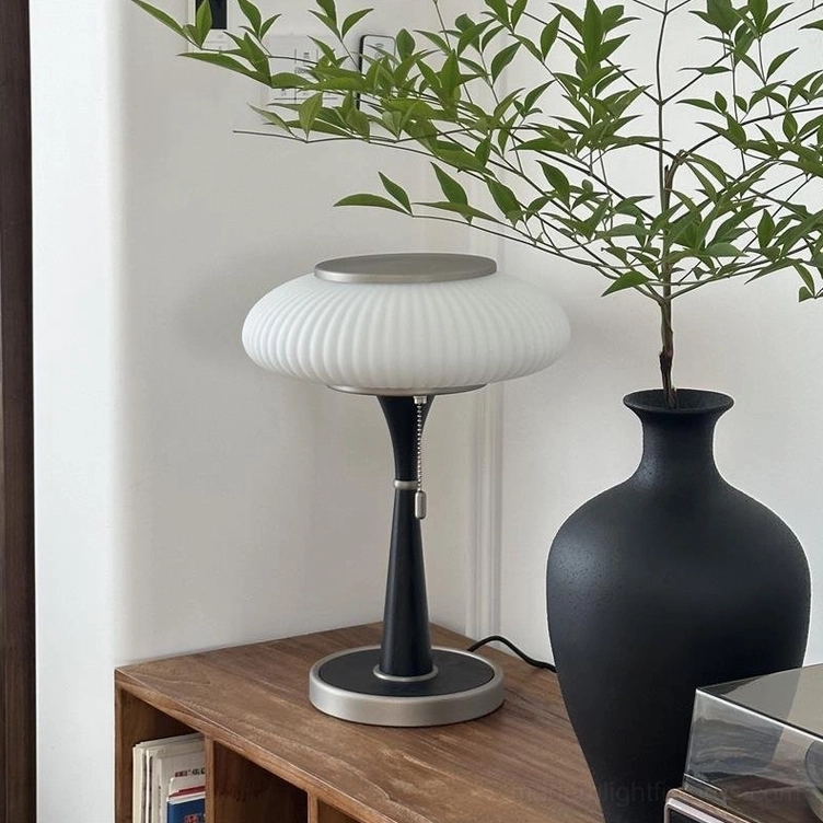 Welma pleated table lamp with black metal pole silver metal base white ribbed shade beside large black ceramic plant vase on wooden bookshelf