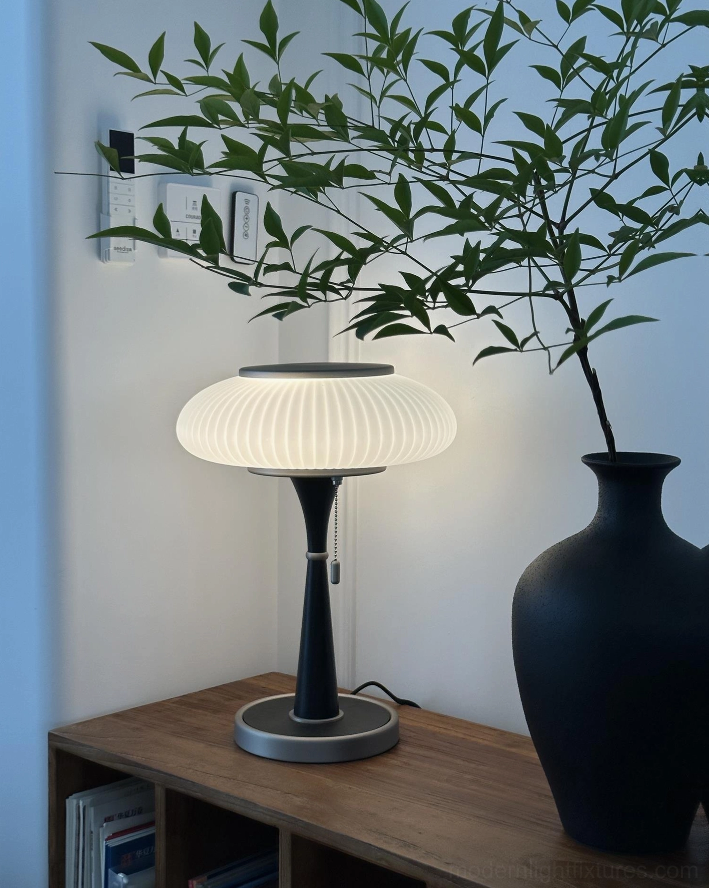 Welma table lamp with white ribbed pleated shade black metal pole silver base beside black ceramic plant vase on living room side table