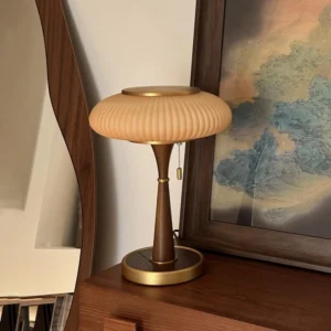 Mid-century modern Welma pleated table lamp with brass trim and dark wood pole displayed on wooden dresser with mirror and landscape art