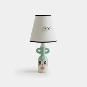 Hand-painted ceramic whimsical table lamp with expressive face base and white fabric shade with black trim featuring 3D kitten accent