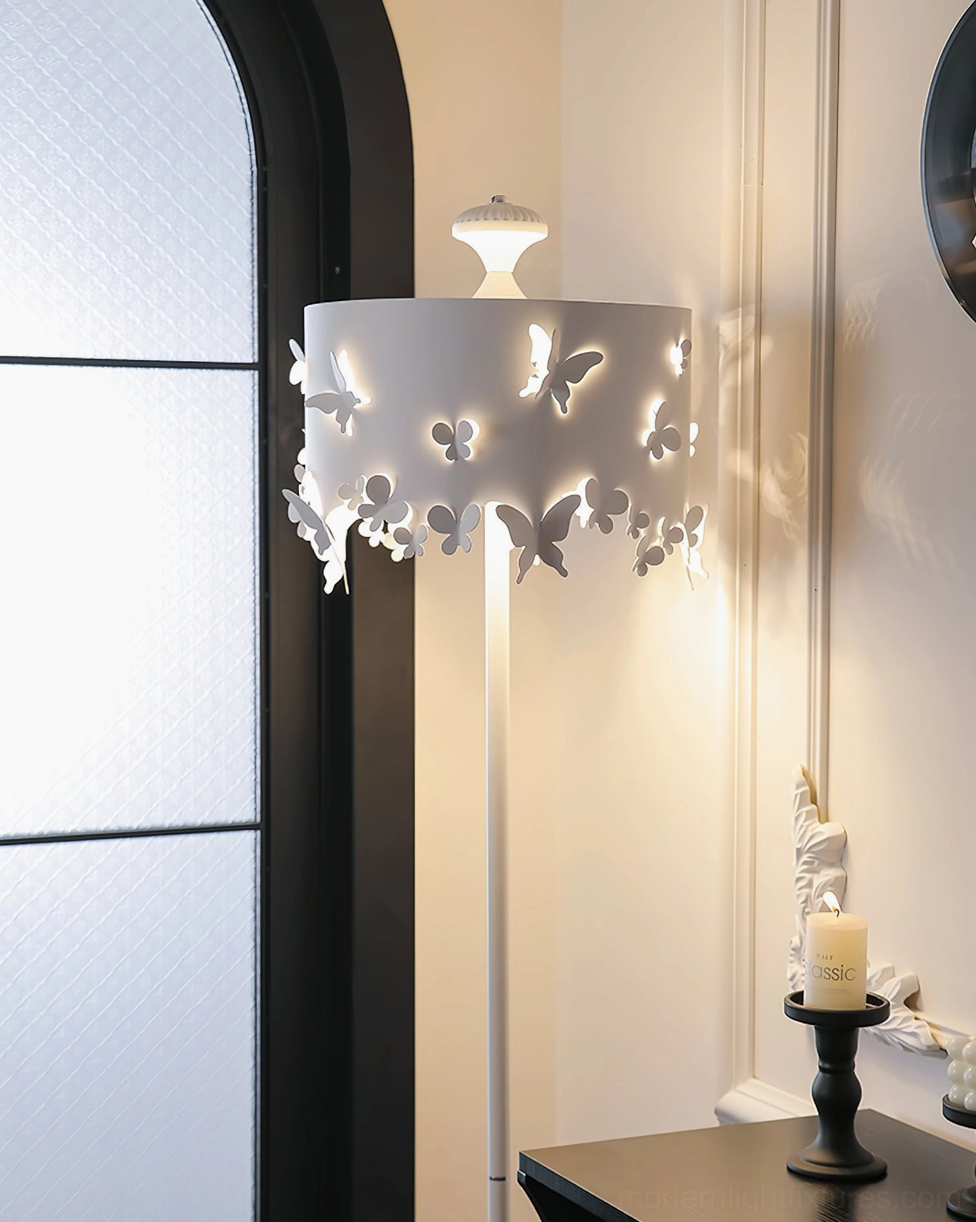 Minimalist white butterfly floor lamp with warm glow casting light patterns on wall, close-up side view