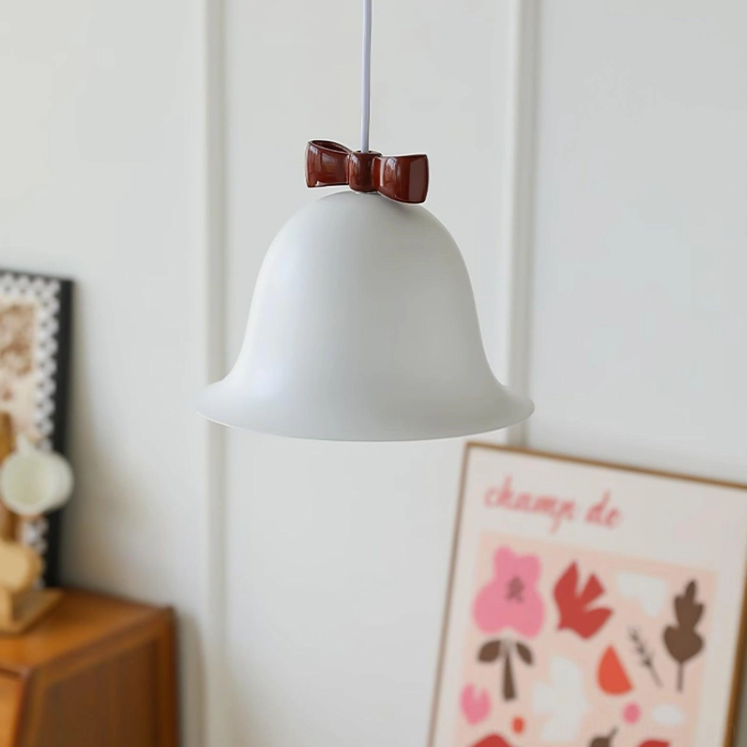 White glossy bell-shaped hanging pendant light with bow detail in home interior with wall art