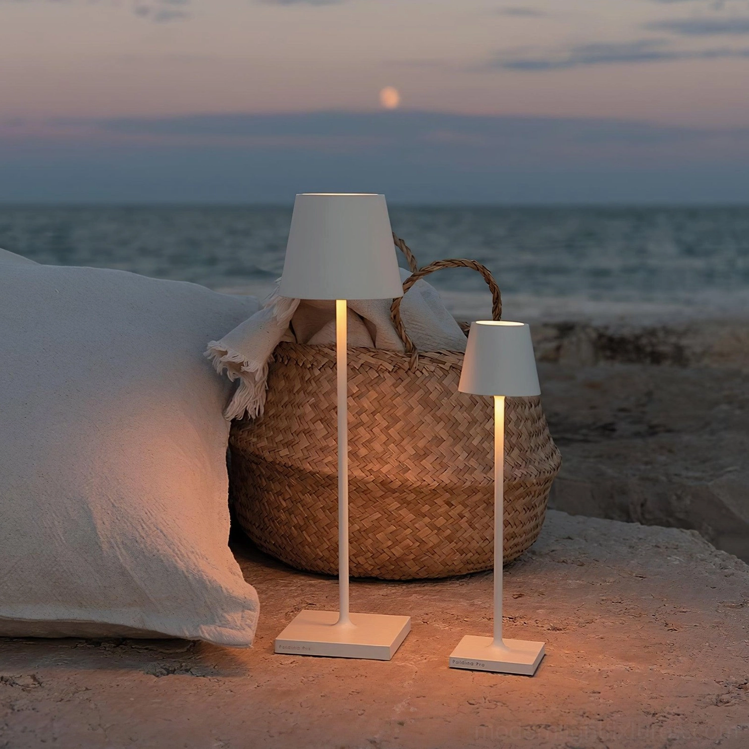 White cordless integrated LED table lamps providing warm ambient lighting on beach seaside night setting with coastal decor