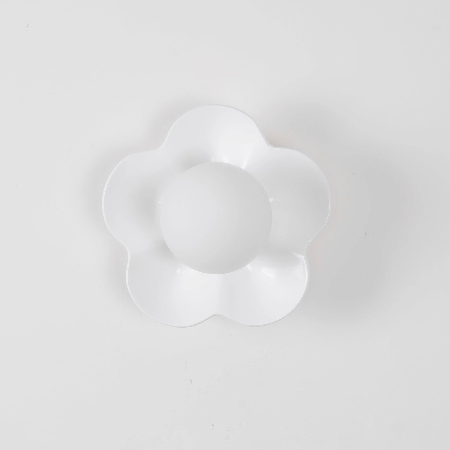 White flower wall sconce with matte petal housing and frosted glass shade on neutral wall