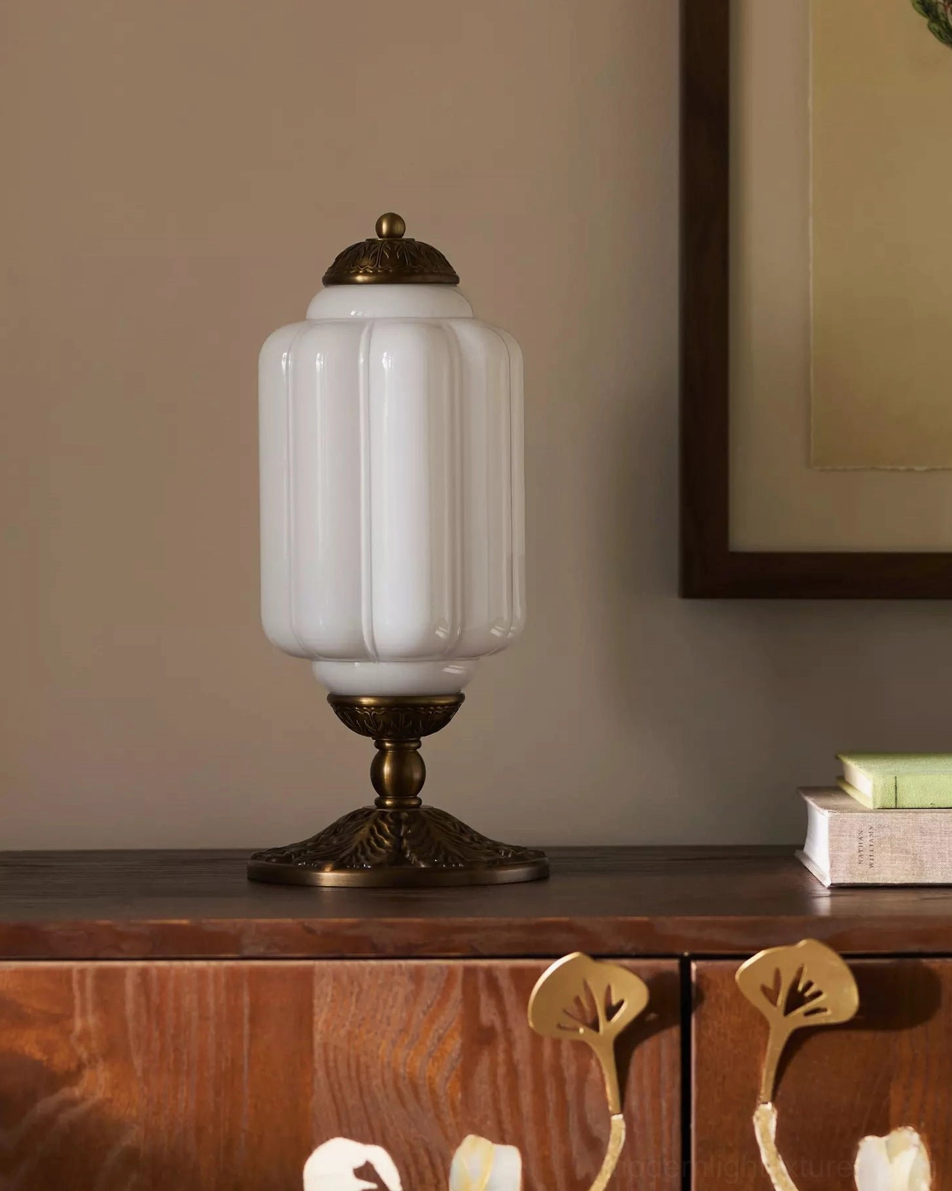 Milky white fluted glass table lamp with bronze base on wooden sideboard with stacked books and framed wall art