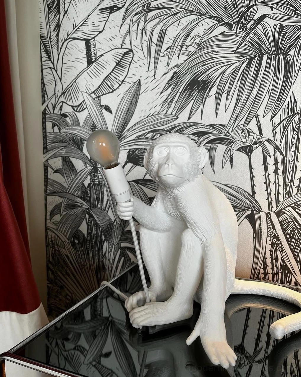White monkey table lamp low front view sitting pose on glass table with tropical wall