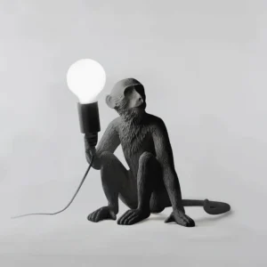 White matte resin monkey table lamp in sitting pose with exposed bulb, front flat studio view