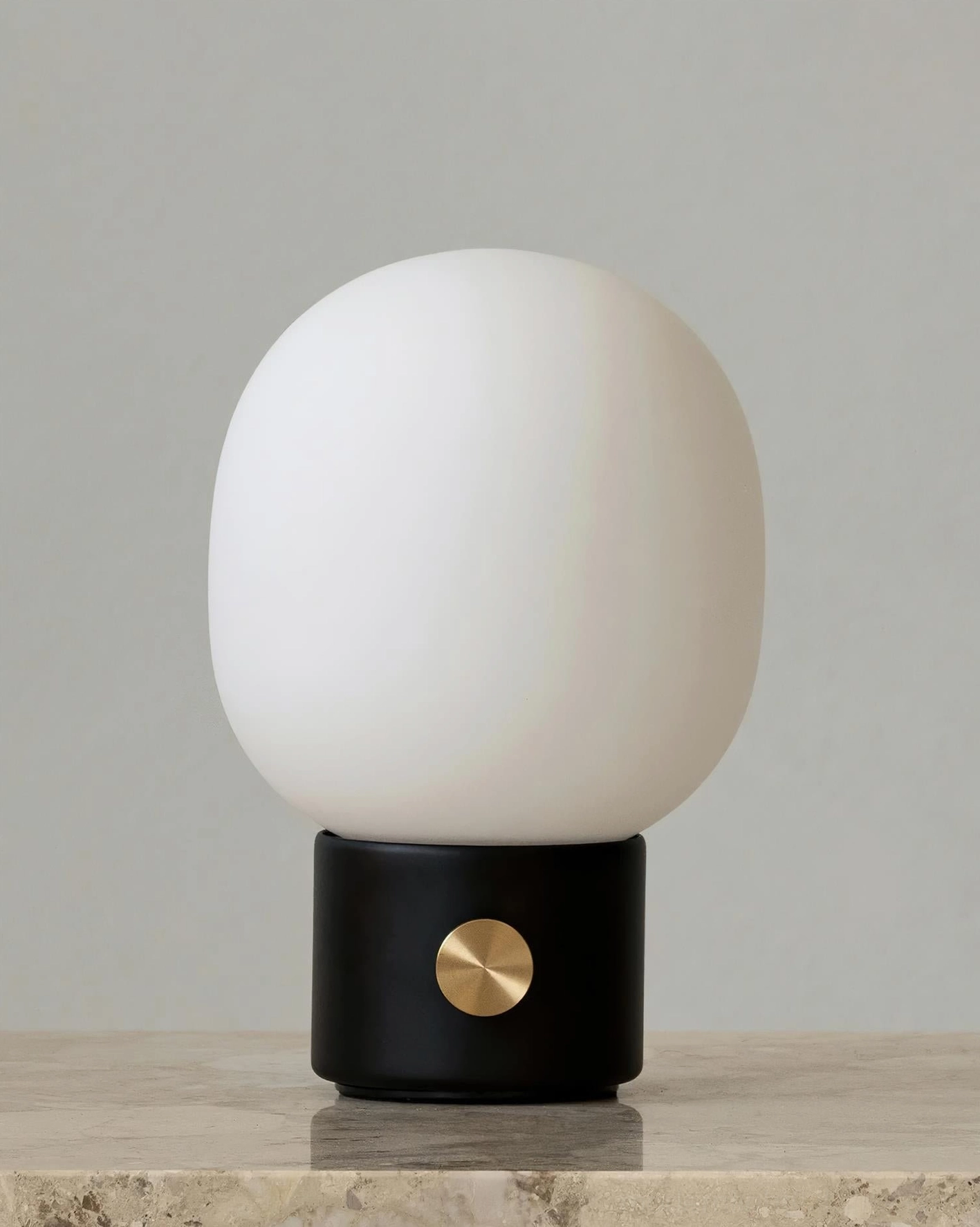 White Monolith table lamp with black metal base and brass switch on neutral stone background