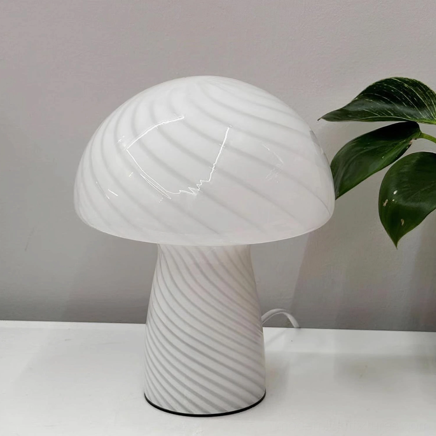 White striped Venetian mushroom glass table lamp front view on minimalist desk with green plant