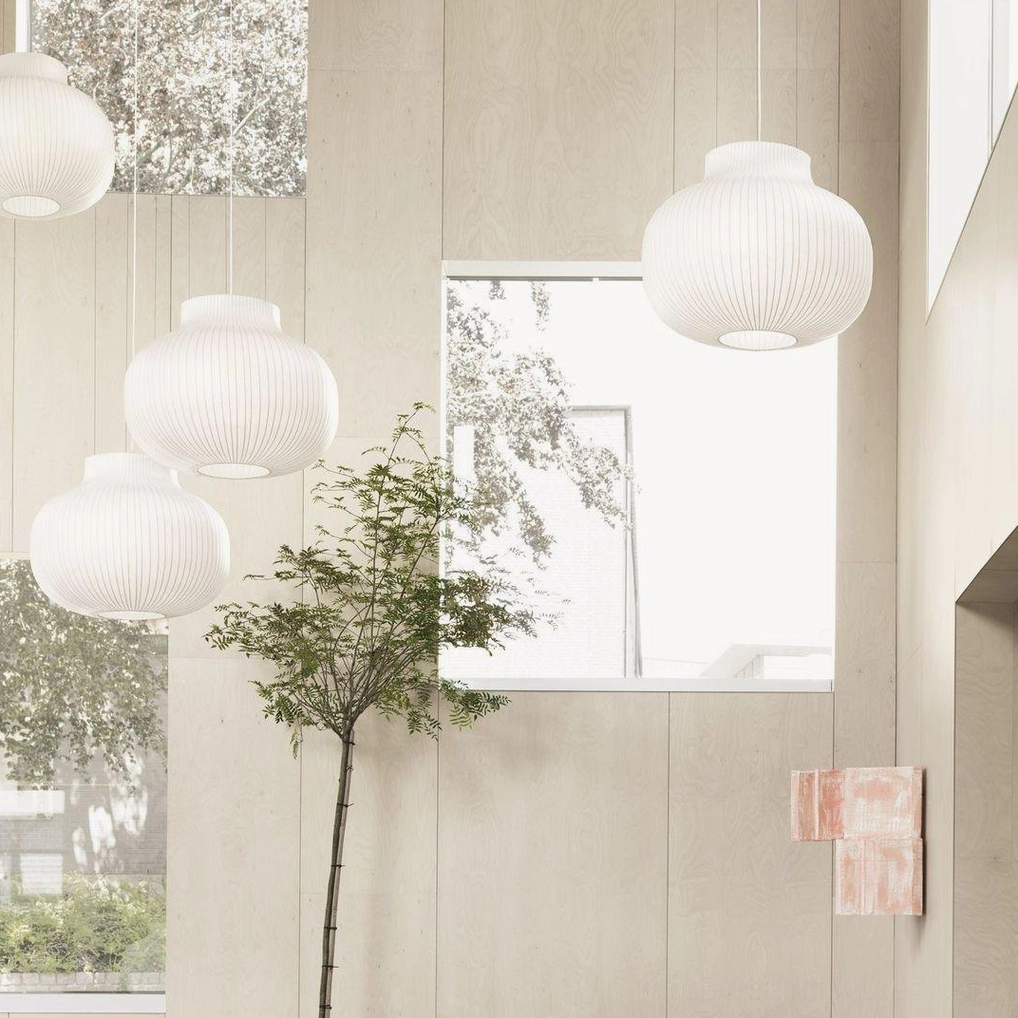 Multiple white fabric cocoon pendant lamps in bright residential living space with high ceilings and indoor plants