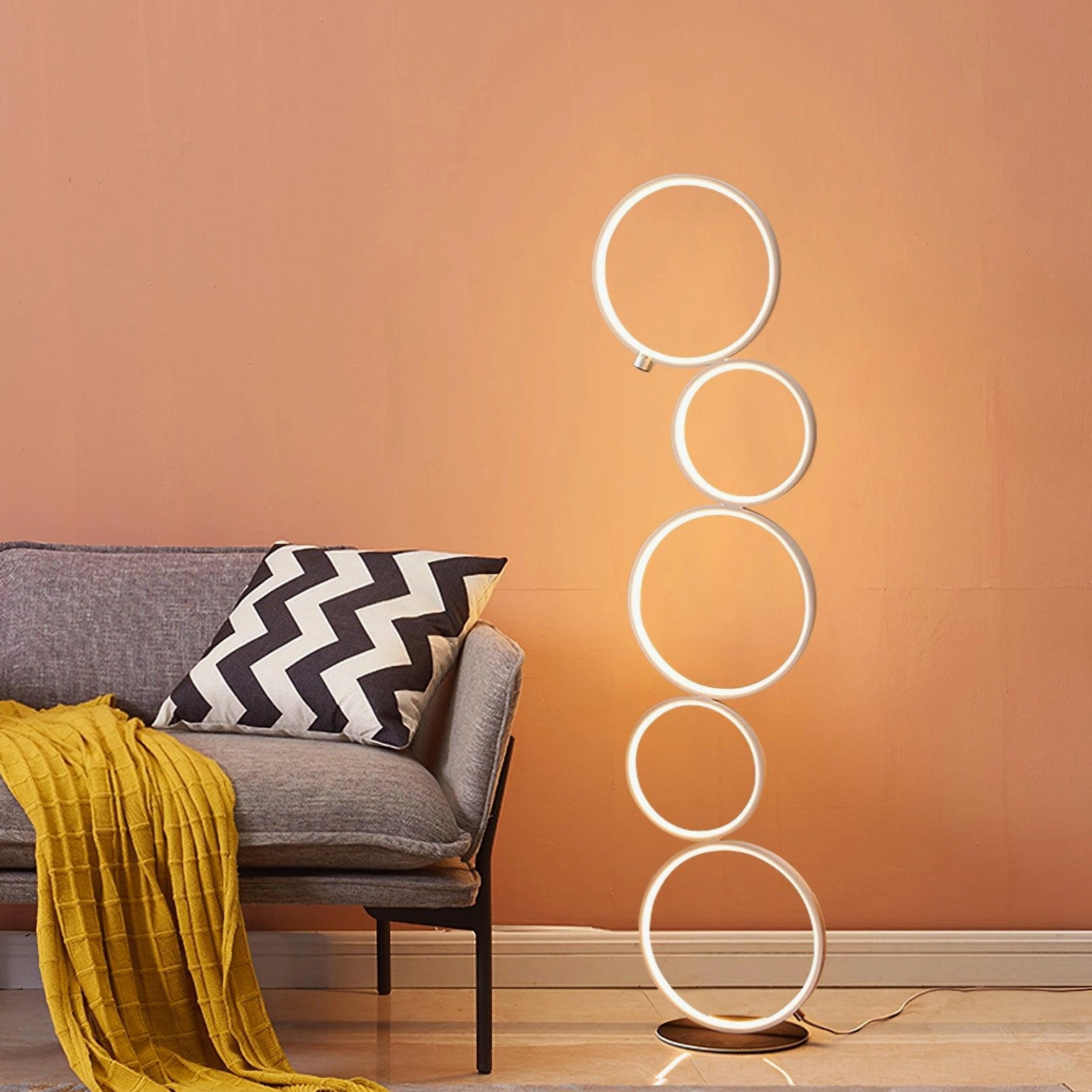 Minimalist white circular LED ring floor lamp with warm ambient lighting in cozy gray sofa living room
