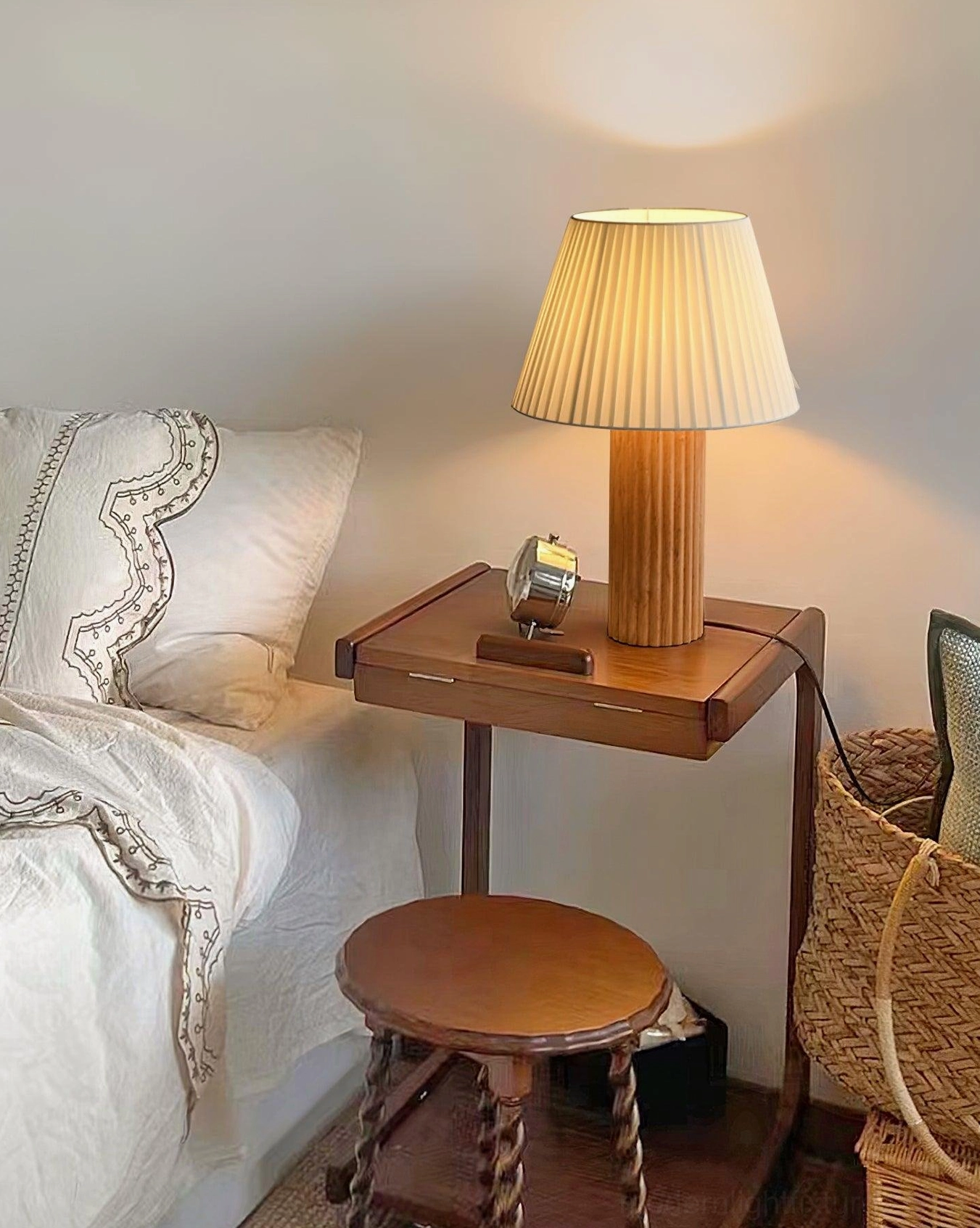 Natural wood base table lamp with warm glowing pleated shade on wooden bedside table in cozy rustic minimalist bedroom setting with bedding