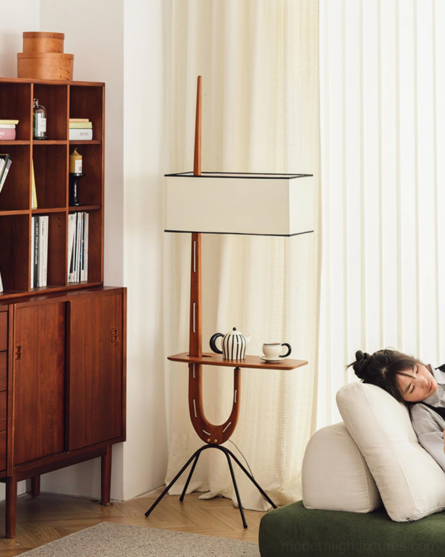 Mid-century style floor lamp with integrated wooden shelf in living room with person relaxing on sofa
